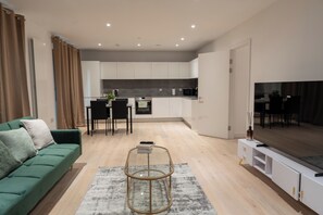 Ein modernes Wohnzimmer mit einem grünen Sofa, einem Glastisch und einem Fernsehschrank.
