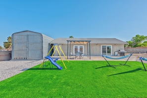 Ein Haus mit Garten, Spielplatz, Hängematte und Gartenhaus.
