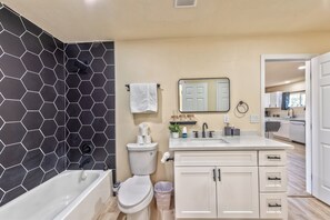 Ein modernes Badezimmer mit Wand aus sechseckigen Fliesen, einer weißen Badewanne, einer Toilette, einem Waschbecken mit Spiegel und einem Schrank.