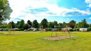 A grassy park with playground equipment, trees, and a clear sky. - Mobile Home Lodge (Bonzée)