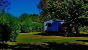 A small, single-story building with a sloped roof, surrounded by dense greenery and trees. - Mobile Home Lodge (Bonzée)