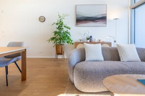 Un salon moderne avec une table à manger en bois, un canapé gris agrémenté de coussins texturés, une plante en pot et un tableau accroché au mur.