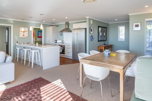 A modern kitchen with white bar stools, a dining table with chairs, and a central island.