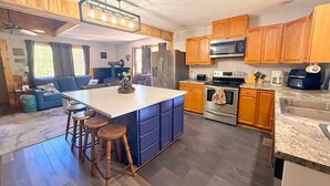 A modern kitchen with wooden cabinets, a central island with stools, a stainless steel refrigerator, and a microwave. - The Buckhorn Lodge in Custer (Custer)