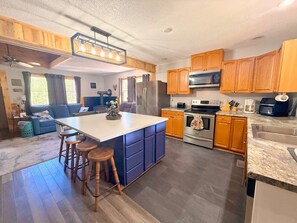 Una cocina moderna con armarios de madera, una isla central con taburetes, un refrigerador de acero inoxidable y un microondas.