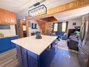 Una cocina moderna con una isla central, detalles de madera y un comedor con sofá y mesa.