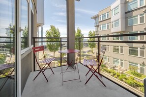 Ein Balkon mit Tisch und Stühlen, großen Fenstern und Blick auf Gebäude und Grünflächen.