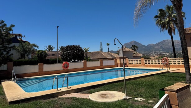 Une piscine équipée d’une bouée de sauvetage, une zone herbeuse et une vue sur les montagnes en arrière-plan.