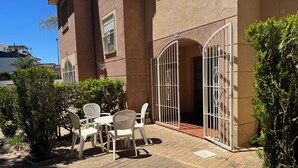 Un espace extérieur aménagé avec une table et des chaises, une entrée fermée par un portail et un bâtiment portant un numéro.