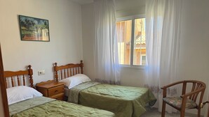 Une chambre avec deux lits, une chaise, une table de chevet, une fenêtre avec des rideaux et un tableau au mur.