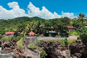 Um resort costeiro com uma ponte de pedra, edifícios com telhados vermelhos e vegetação exuberante.
