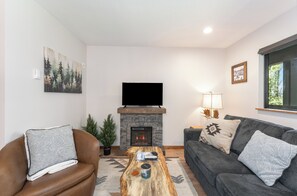 A living room with a fireplace, a television, a couch, and a coffee table. - New! Cozy Condo at Marina Cay | Flathead Lake, Glacier & Bigfork Village (Bigfork)