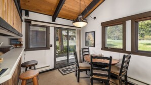 A dining area with a wooden table and chairs, a pendant light, and large windows with a view of greenery. - Nordic Pines Retreat | Ski, Golf & Unwind (Big Sky)