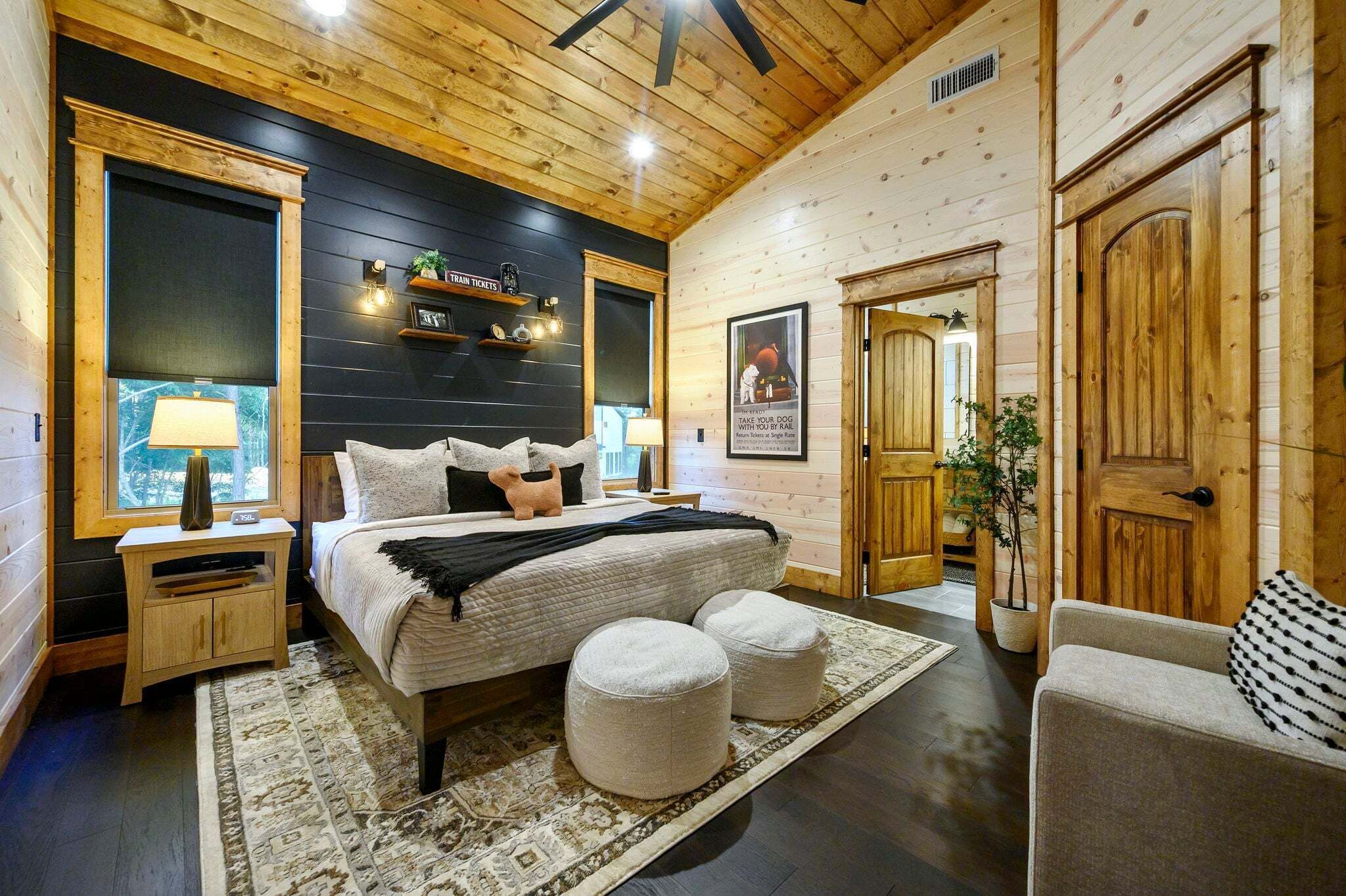 Une chambre confortable dans un chalet en bois, avec un lit, des tables de chevet, une lampe, une fenêtre, une porte et une affiche encadrée.