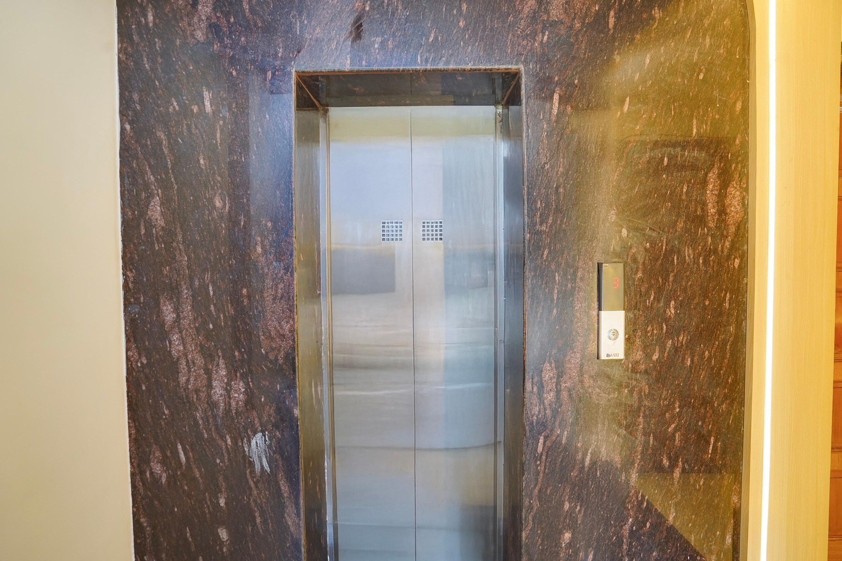 An elevator with a metallic finish and a control panel on the wall beside it.