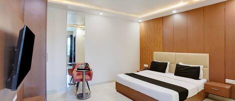 A modern hotel room with a large bed, bedside tables, a TV, and a small seating area with a table and chairs.