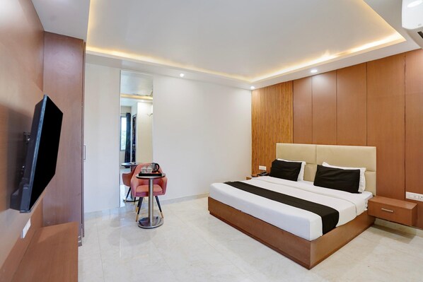 A modern hotel room with a large bed, bedside tables, a TV, and a small seating area with a table and chairs.