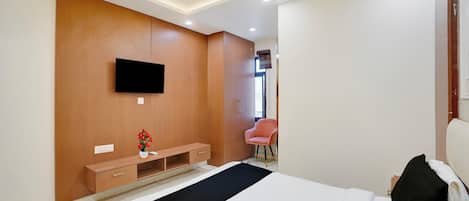 A modern bedroom with a bed, a TV mounted on the wall, a small wooden cabinet, and a chair.