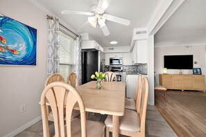 Ein Essbereich mit Holztisch, Stühlen, einem Deckenventilator, einer Küche im Hintergrund und einem Fernseher auf einem Schrank.