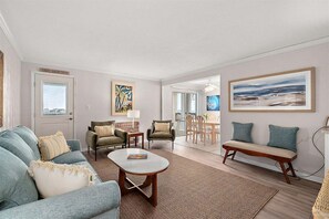 Ein Wohnzimmer mit einer Couch, Sesseln, einem Couchtisch und einem Essbereich mit Tisch und Stühlen.