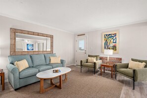 Ein Wohnzimmer mit einer Couch, Sesseln, einem Couchtisch, einem Kamin, einem Spiegel und einem Gemälde.