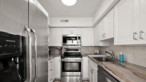 Een moderne keuken met roestvrijstalen apparatuur, witte kastjes en een marmeren aanrecht.