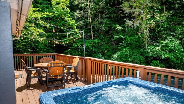 Une terrasse en bois avec un jacuzzi, du mobilier d’extérieur et une vue sur une forêt.