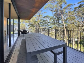 An outdoor deck with a table and chairs, surrounded by a railing, overlooking a forested area. - Coastal Sanctuary near Beaches & Bush Tracks (Rosedale)