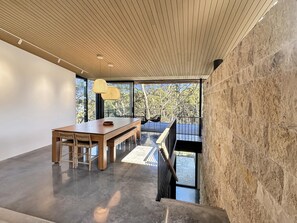 A modern interior with a wooden dining table, chairs, and a bench, a staircase, and a view of trees through large windows. - Coastal Sanctuary near Beaches & Bush Tracks (Rosedale)