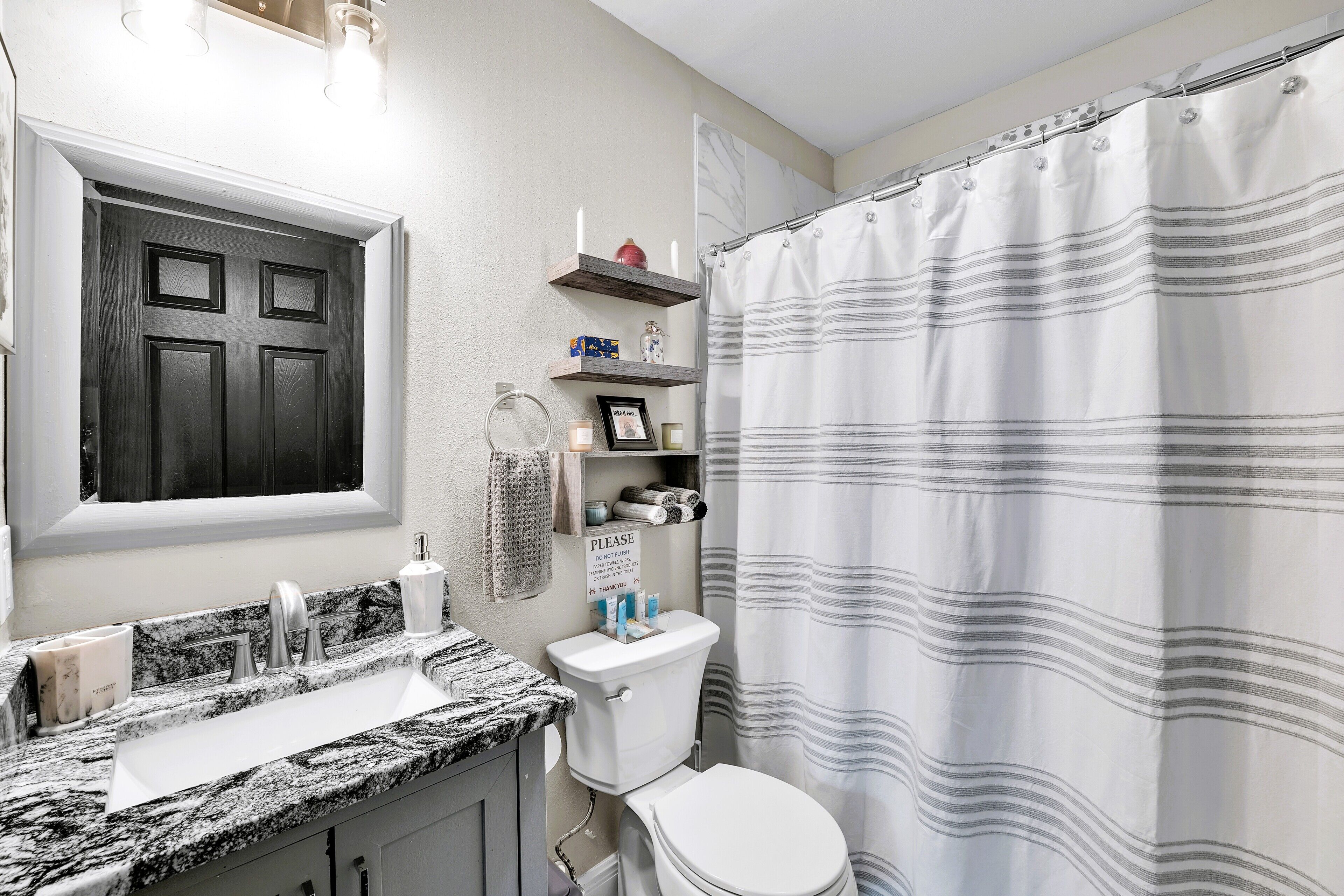 Un baño con puerta negra, un lavabo blanco con encimera de granito, inodoro y cortina de ducha a rayas.
