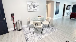 A modern dining area with a glass table, white chairs, a patterned rug, and a stainless steel trash can. - Modern Luxe Retreat - Fully Furnished Short-Term Rental in Lakeland (Lakeland)