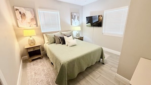 A bedroom with a bed, two bedside tables, a ceiling fan, a TV, and two windows with blinds. - Modern Luxe Retreat - Fully Furnished Short-Term Rental in Lakeland (Lakeland)