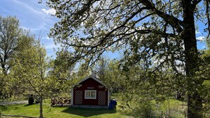 Un petit bâtiment rouge avec une fenêtre blanche, entouré d’arbres et d’une zone herbeuse.