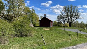 Une grange rouge avec une cheminée, entourée d’herbe verte et d’arbres.