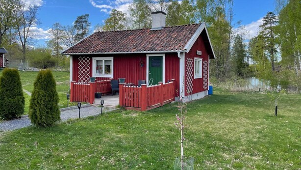 Une cabane en bois rouge avec un toit en tuiles, une véranda avec des sièges et un petit jardin.