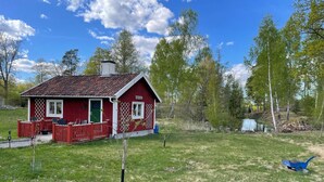 Une maison en bois rouge avec une véranda entourée d’une clôture et un petit jardin.