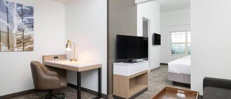 A hotel room with a desk, chair, TV, bed, and a view of the outside.