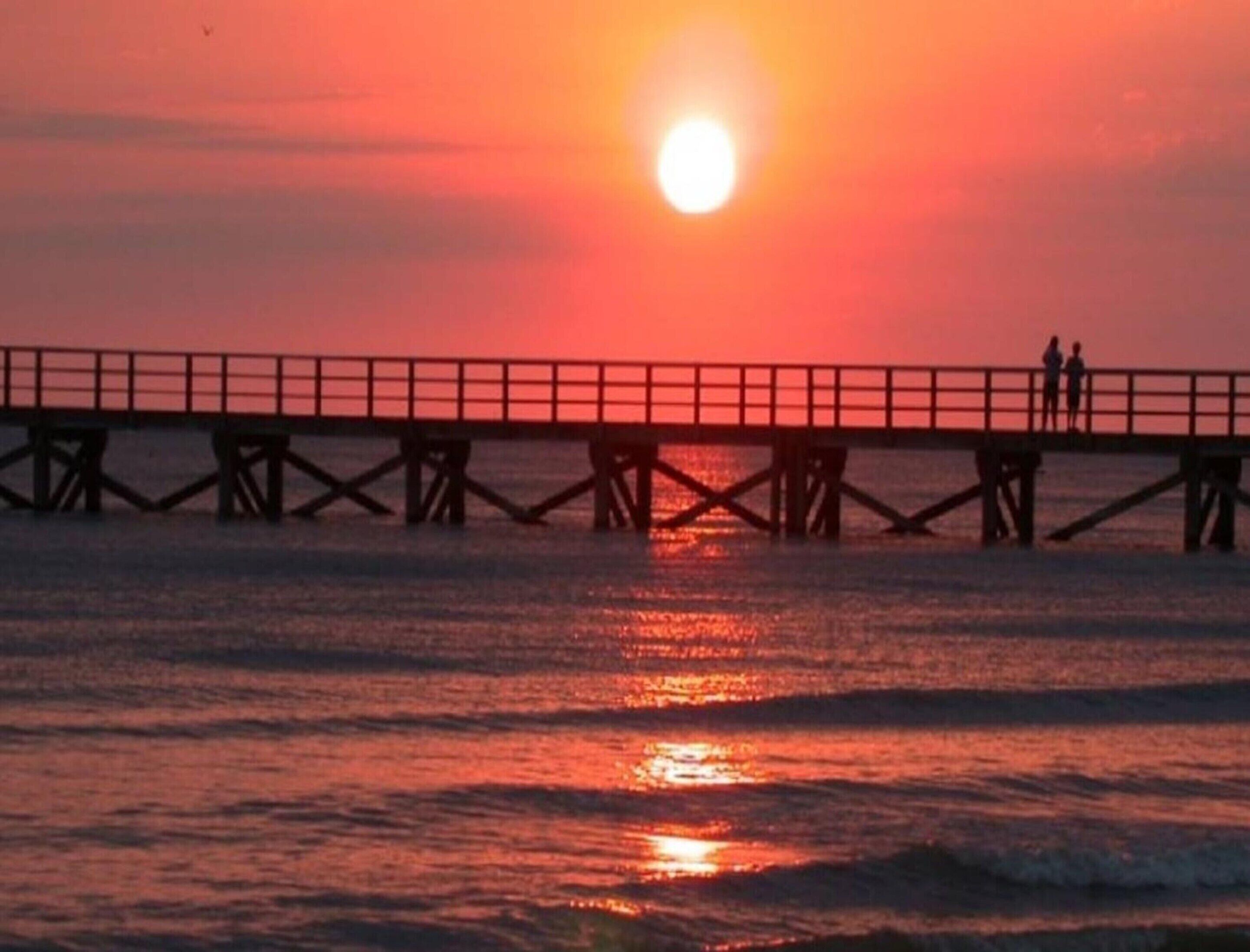 Un muelle que se extiende sobre el agua, con un atardecer de fondo.