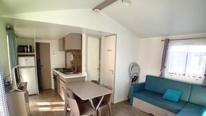 A compact living space with a kitchenette, a dining table, a sofa, and a window with curtains. - Cosy Retreat Near Saint-jean-de-monts (Saint-Jean-de-Monts)