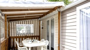 A covered patio with a table and chairs, a window, and a door leading to a house. - Cosy Retreat Near Saint-jean-de-monts (Saint-Jean-de-Monts)