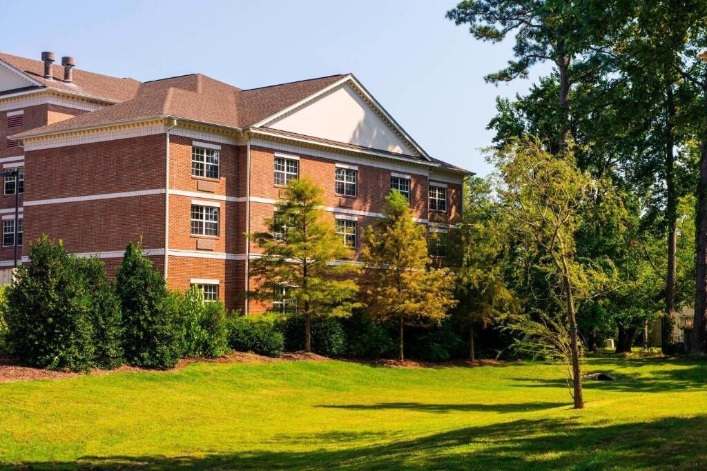 A multi-story brick building with a flat roof, surrounded by a well-maintained lawn and trees.