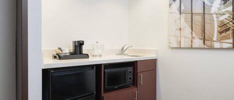 A compact kitchenette with a refrigerator, microwave, sink, and coffee maker.