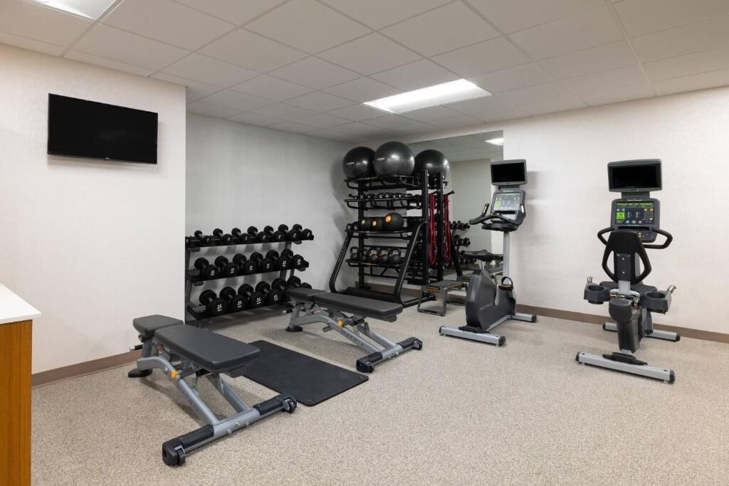 Une salle de sport équipée de matériel de musculation, de tapis de course et d’un téléviseur fixé au mur.