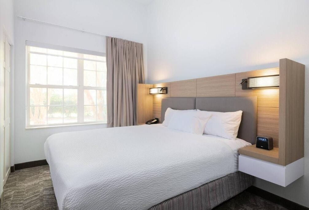 A hotel room with a large bed, a bedside table with a lamp, a phone, and a wall-mounted light.