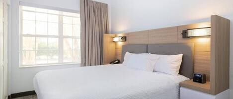 A hotel room with a large bed, a bedside table with a lamp, a phone, and a wall-mounted light.