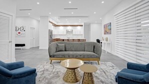 Una sala de estar moderna con un sofá gris, dos mesas redondas para café y sillones azules.