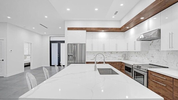 Una cocina moderna con una isla grande, electrodomésticos de acero inoxidable y armarios blancos.