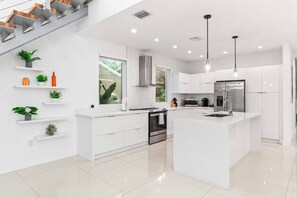 A modern kitchen with white cabinetry, a central island, stainless steel appliances, and a staircase with wooden steps. - 2020 Built Modern Luxe Home Heated Pool & Jacuzzi (Hollywood)