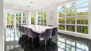 Ruime eethoek met een grote tafel, moderne stoelen en grote ramen met uitzicht op groen.