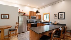 A modern kitchen with stainless steel appliances, wooden cabinets, and a central island with bar stools. - Pet-Friendly Saugatuck Cottage | Hot Tub • Fire Pit • Dog Park (Saugatuck)